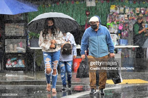 People cross a street under heavy rain in Los Angeles, California on October 25, 2021. - Severe thunderstorms bringing record rainfall hit northern...