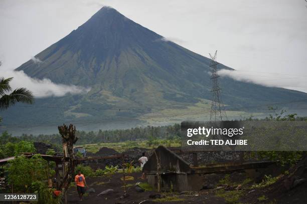 This photo taken on October 5, 2021 shows residents walking past a house half-buried by sand and rock from Mayon volcano were displaced after heavy...