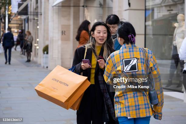 Fashion conscious young women, one with Louis Vuitton orange shopping bags, greet each other on Bond Street which is busier than any time over the...