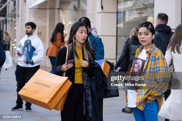 Fashion conscious young women, one with Louis Vuitton orange shopping bags, greet each other on Bond Street which is busier than any time over the...