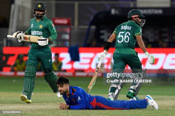 Afghanistan's Rashid Khan falls on the ground as Pakistan's captain Babar Azam and teammate Mohammad Hafeez run between the wickets during the ICC...