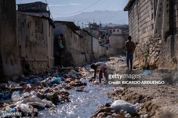 Girl collects water with a bucket from a stream of heavy contaminated water filled with trash in Port-au-Prince, Haiti, on October 29, 2021. -...