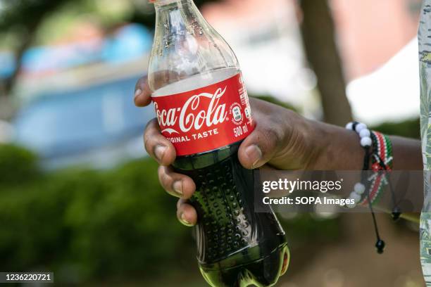 In this photo illustration a hand holds a Coca-cola soft drink. An average of 38% of plastic waste collected near Lake Nakuru National Park, a UNESCO...