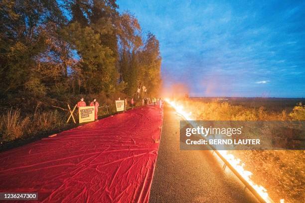 Greenpeace activists stand next to a symbolical red line bordered with fire on the edge of the Garzweiler lignite open cast mine near Luetzerath,...