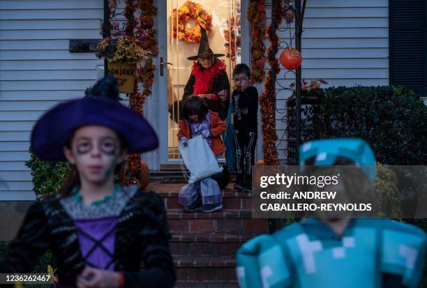 Woman dressed as a witch stays behind her glass door, as a Covid-19 precaution, as children get candy from her front porch while they trick or treat...