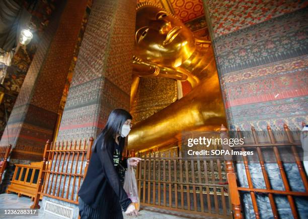 Woman wearing a face mask walks in front of a statue of a reclining Buddha at Wat Pho during the reopening. Thailand has opened its doors to tourists...