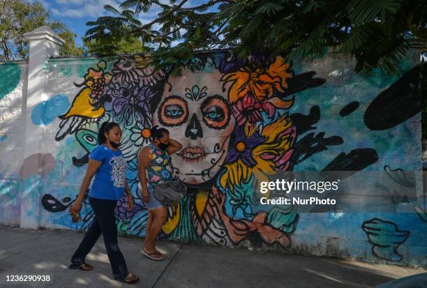 People walk past a mural related to the Day of the Dead on the wall surrounding the municipal cemetery of Playa del Carmen. All Saints' Day in Mexico...