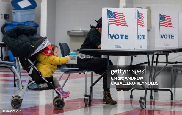 Voter fills in her ballot as her child tries to put a snack on a table at a school cafeteria being used as a polling location on election day in...