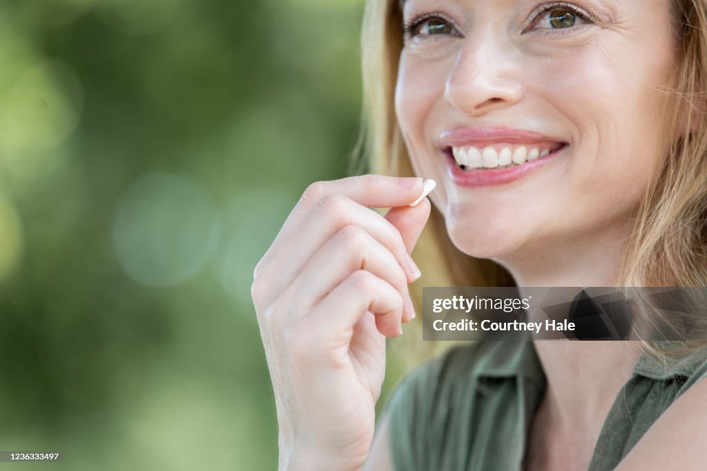 Lächelnde Frau hält Vitamin bis zum Mund