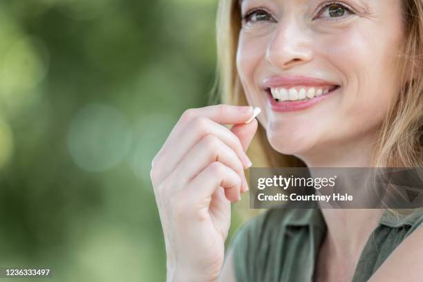 la femme de sourire tient la vitamine jusqu’à la bouche - complément vitaminé photos et images de collection