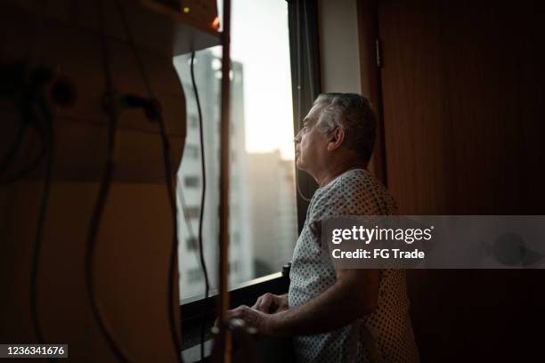 hogere patiënt die door venster bij het ziekenhuis kijkt - geduld stockfoto's en -beelden