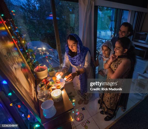 Navjeet Kaur, along with daughters Meher, 8 and Samieen, 11 and husband, Gurjog Singh, light candles in the familys home in front of a small altar in...