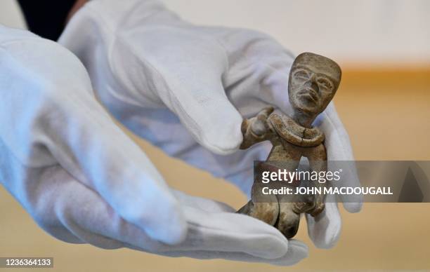 Two hands wearing white gloves hold and present a "Kneeling Figure" during a handing over ceremony of a small trove of Mayan cultural artefacts being...