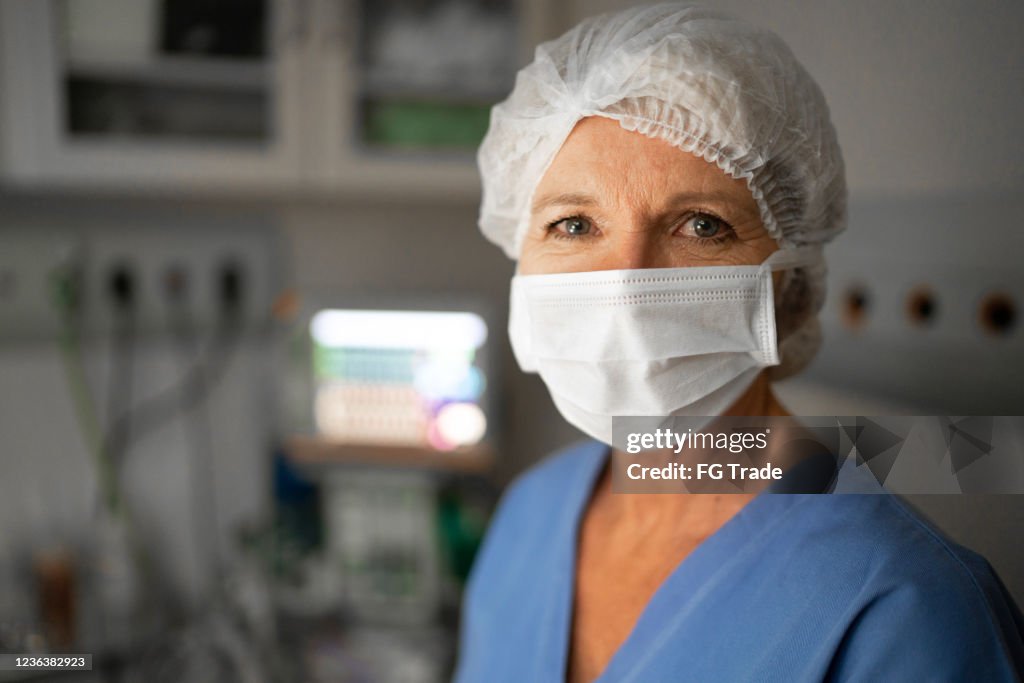 Portret van vrouwelijke gezondheidsarbeider met gezichtsmasker op werkende ruimte bij het ziekenhuis