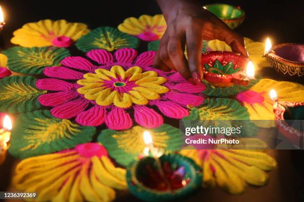 Hindu woman places a diya on a colourful rangloli design that was created using coloured powder during the festival of Diwali at a Hindu temple in...