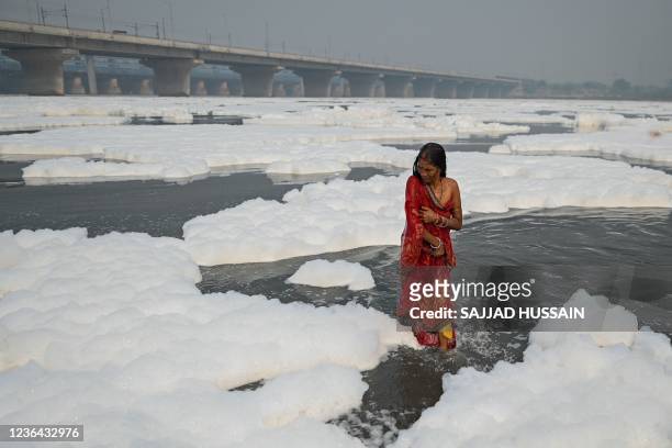 Devotee takes a dip in the waters of Yamuna river as a part of rituals for the upcoming Hindu festival of Chhat puja amid foam created by pollution...