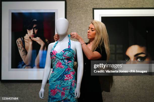 Bonhams gallery assistant adjusts Amy Winehouse's blue Hawaiian dress worn on stage by Amy on stage in Brazil in 2011 , with photographs of her by...