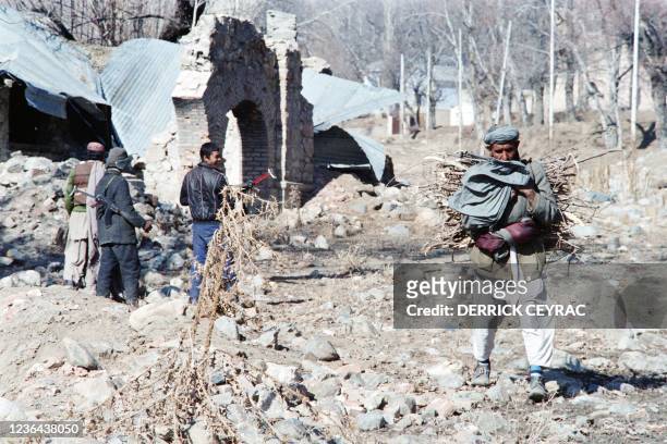 An old Afghan man, carrying wood on his back, passes by militiamen of Afghan regular army who guard Paghman village which was mainly destroyed during...