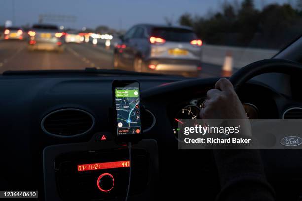 Seen from the passenger seat of a car, winter light fades into darkness through the windscreen whose driver is using Google Maps to navigate...