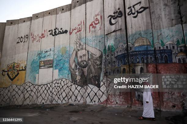 Palestinian man walks alongside Israel's separation barrier painted with an image of jailed Fatah leader Marwan Barghuti, in the West Bank town of...