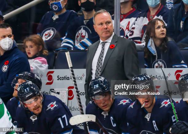 Assistant coach Dave Lowry of the Winnipeg Jets looks on from the bench while standing behind his son Adam Lowry with teammates Blake Wheeler and...