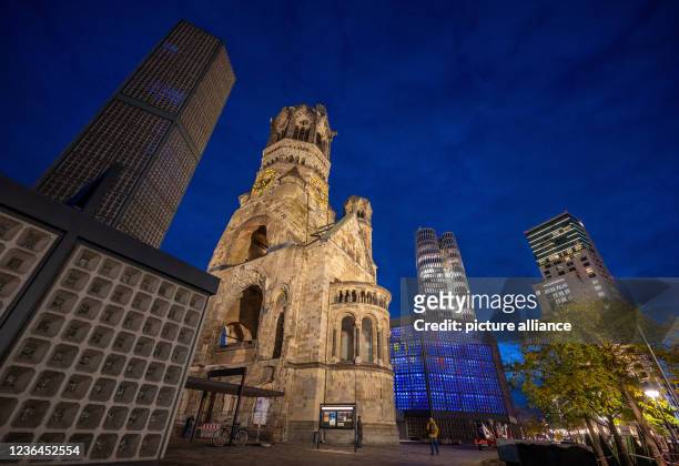 November 2021, Berlin: The old and new towers of the Kaiser Wilhelm Memorial Church rise into the evening sky against the backdrop of modern...