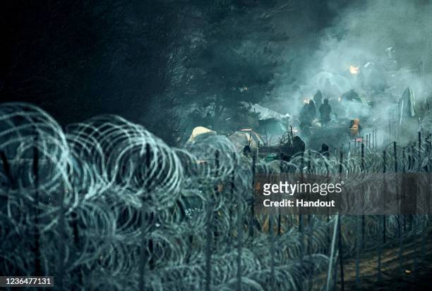 In this handout image issued by the Polish Ministry of National Defence, migrants are seen behind barbed wire on the Belarus-Polish border on...