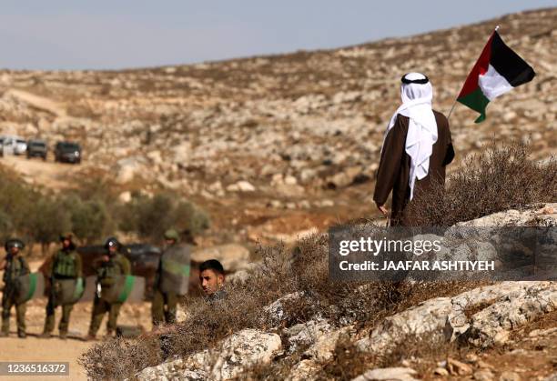 Palestinian protester raises a national flag as he stands facing Israeli security forces, during a demonstration against the establishment of Israeli...