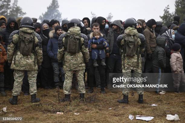 Migrants stand in front of Belarusian servicemen as they gather in a camp near the Belarusian-Polish border in the Grodno region on November 14,...