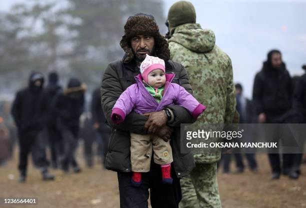 Migrant carrying a child walks in a camp near the Belarusian-Polish border in the Grodno region on November 14, 2021. - Dozens of migrants have been...
