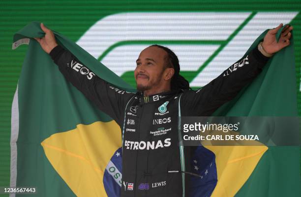 Mercedes' British driver Lewis Hamilton holds a Brazilian flag as he celebrates on the podium after winning Brazil's Formula One Sao Paulo Grand Prix...