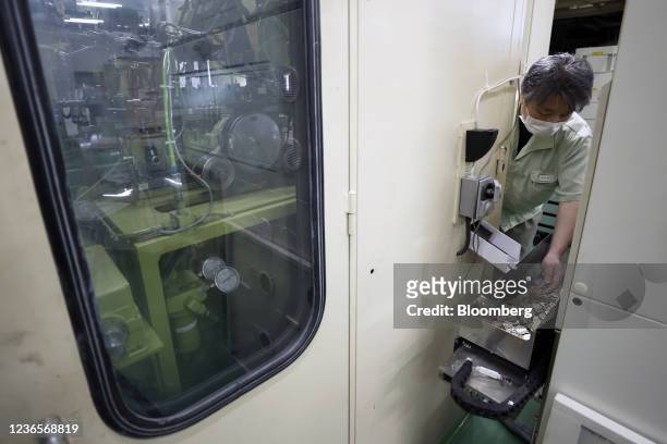 An employee inspects a newly-stamped Japanese 500 yen coin in front of a coining press, left, during the production at a Japan Mint factory in...