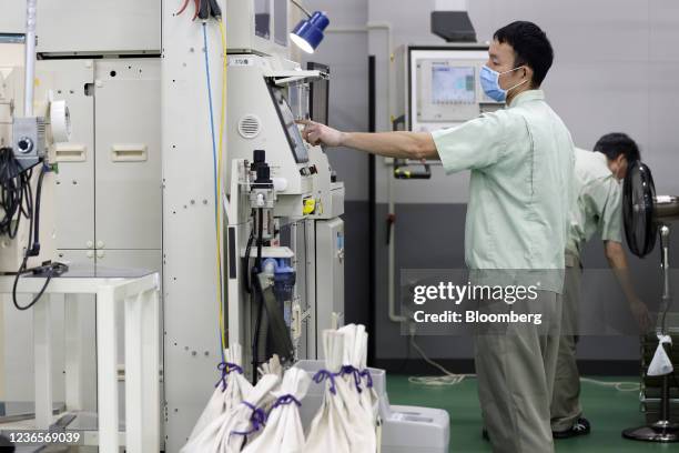 An employee operates a coin inspection machine, front, during the production of new Japanese 500 yen coins at a Japan Mint factory in Saitama, Japan,...