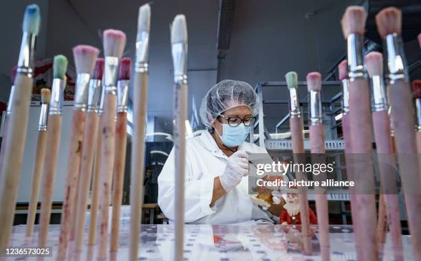 November 2021, Schleswig-Holstein, Lübeck: A worker paints a marzipan Santa Claus with food colouring in a production hall at Niederegger. Christmas...