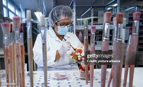 November 2021, Schleswig-Holstein, Lübeck: A worker paints a marzipan Santa Claus with food colouring in a production hall at Niederegger. Christmas...