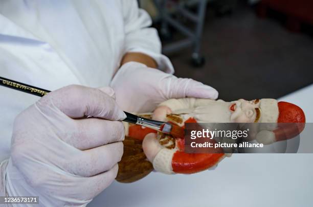 November 2021, Schleswig-Holstein, Lübeck: A worker paints a marzipan Santa Claus with food colouring in a production hall at Niederegger. Christmas...