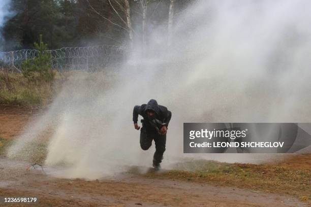 Man runs away from a water cannon used by Polish law enforcement officers against migrants attempting to break into Poland at the Bruzgi-Kuznica...