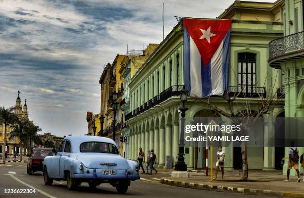 An old American car rides near a Cuban flag hanging from a building in Havana, on November 17, 2021. - A planned demonstration in the Havana was...