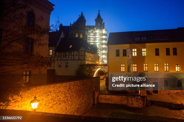 November 2021, Saxony-Anhalt, Magdeburg: A scaffolding covered with a tarpaulin shines brightly at nightfall at the cathedral. Above it, an almost...