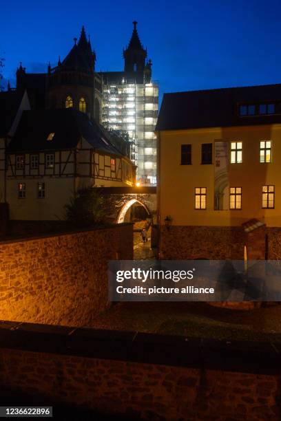 November 2021, Saxony-Anhalt, Magdeburg: A scaffolding covered with a tarpaulin shines brightly at nightfall at the cathedral. Above it, an almost...