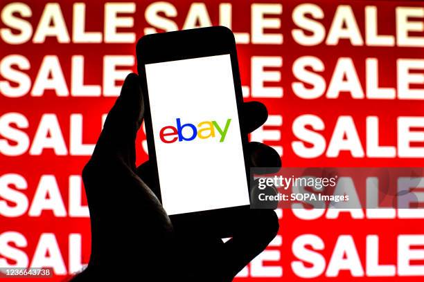 In this photo illustration, an eBay logo is seen on a smartphone screen with 'Sale' words in the background.