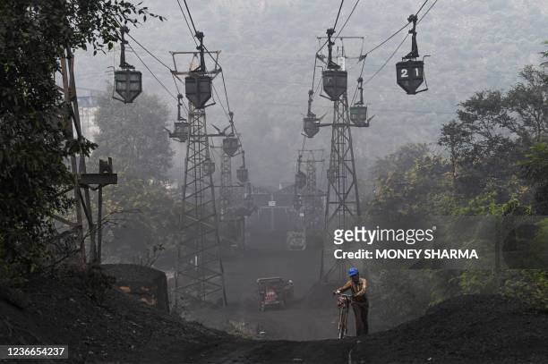Worker pushes his bicycle under a line of cable trolleys transporting coal in Sonbhadra, Uttar Pradesh, on November 19, 2021.
