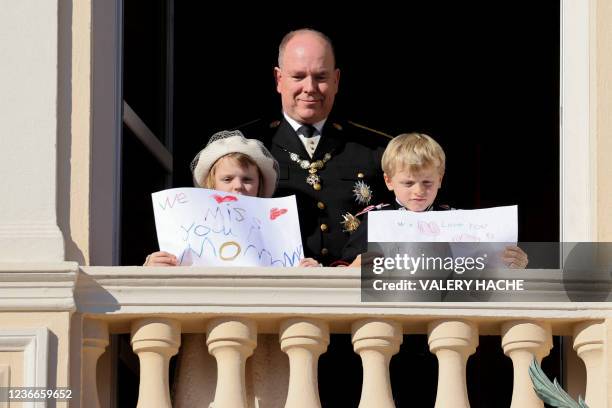 Prince Albert II of Monaco, Princess Gabriella and Prince Jacques stand with a message for Princess Charlene at the balcony of Monaco Palace during...