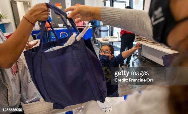 Moises Sanchez, middle, age 3, reaches up as his mother receives fresh vegtables. Through a jointly-operated Community Resource Center, L.A. Care...