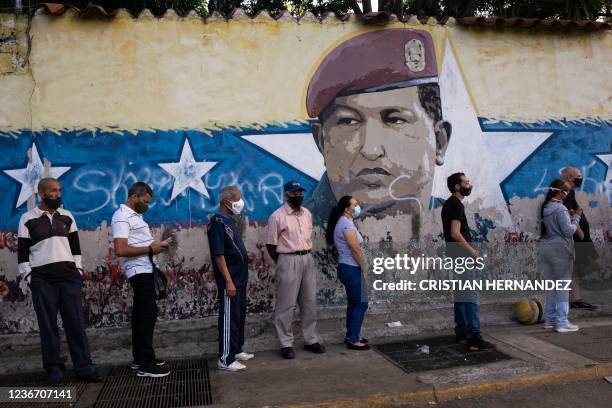 People queue at a polling station in Caracas, next to a mural depicting late Venezuelan President Hugo Chavez, during regional and municipal...