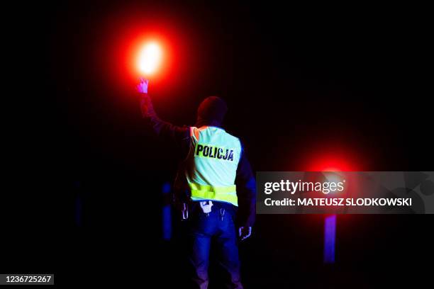 Police officer holds up lights to check vehicles entering the state of emergency area at a checkpoint near the village of Bialowieza, eastern Poland,...