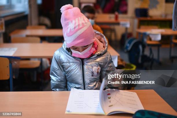 Girl wears a hat, a face mask and a winter jacket as she attends lessons in her aerated classroom at the Petri primary school in Dortmund, western...
