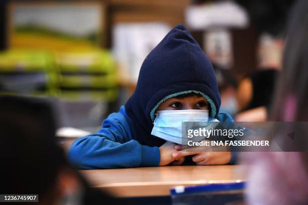 Boy wears a hat and a face mask as he attends lessons in his aerated classroom at the Petri primary school in Dortmund, western Germany, on November...