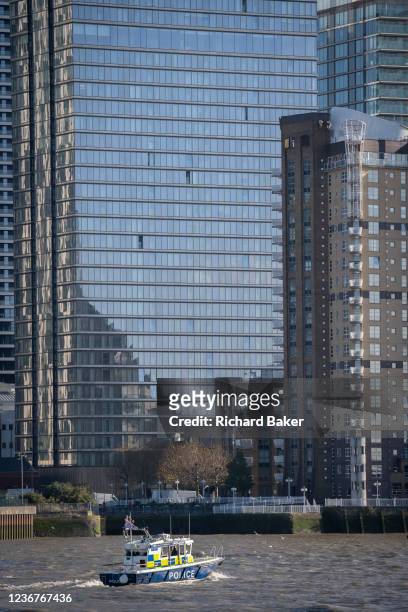 Boat from the Met police's Marine unit patrols the waters of the river Thames beneath the tall office buildings of London Docklands at Canary Wharf,...