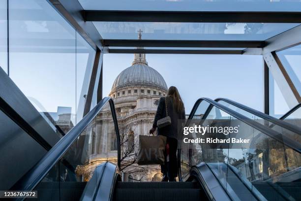 Woman holds shopping bags as she ascends the escalator from a shopping mall beneath St Paul's Cathedral in the City of London, the capital's...